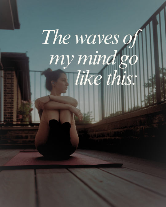 A woman seated on a yoga mat in a balcony, hugging her knees, looking at her left